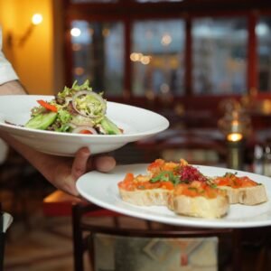 A waiter serves a fresh salad and hors doeuvres in a cozy restaurant setting.